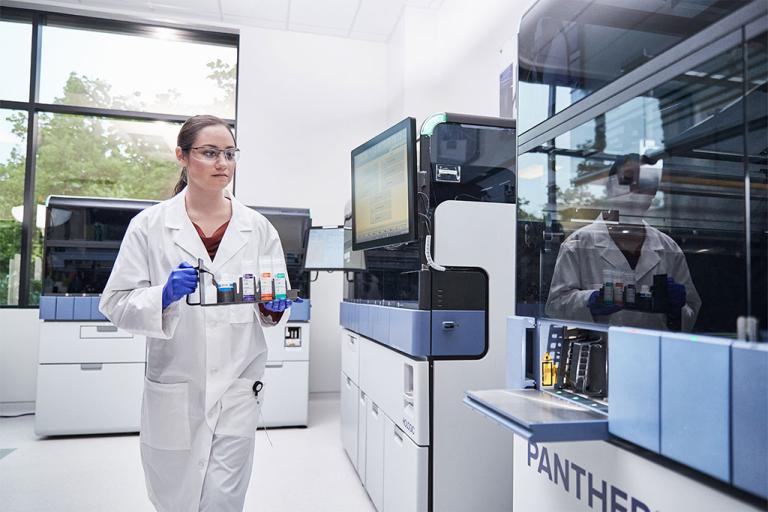 Technicienne de laboratoire portant un plateau d’échantillons à insérer dans le système Panther