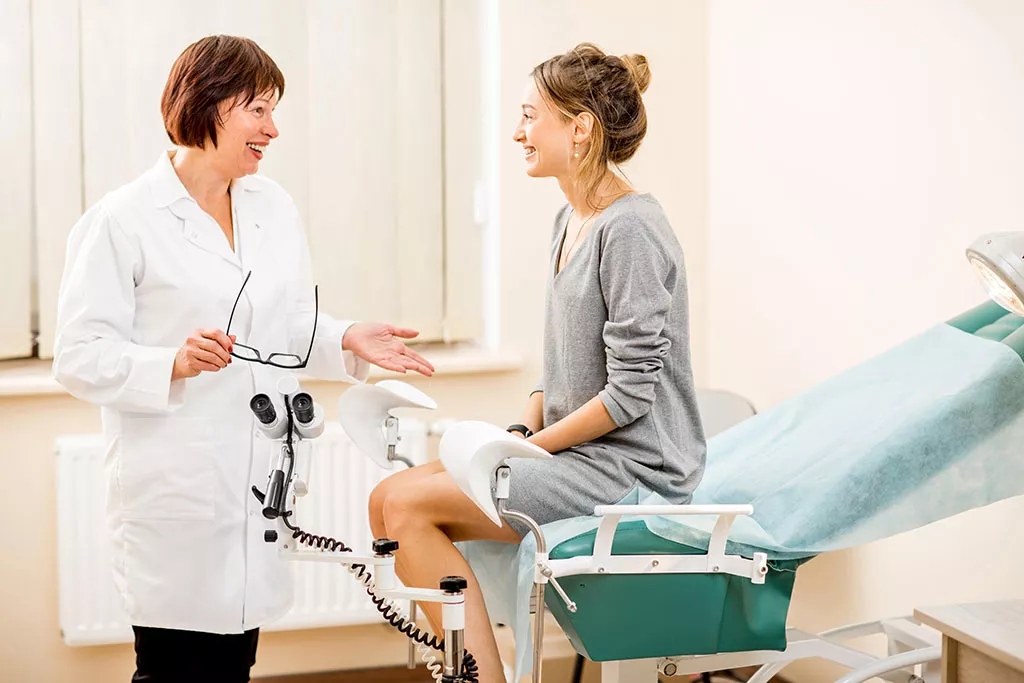 Patiente assise sur une table d’examen à l’hôpital, s’entretenant avec une professionnelle de santé
